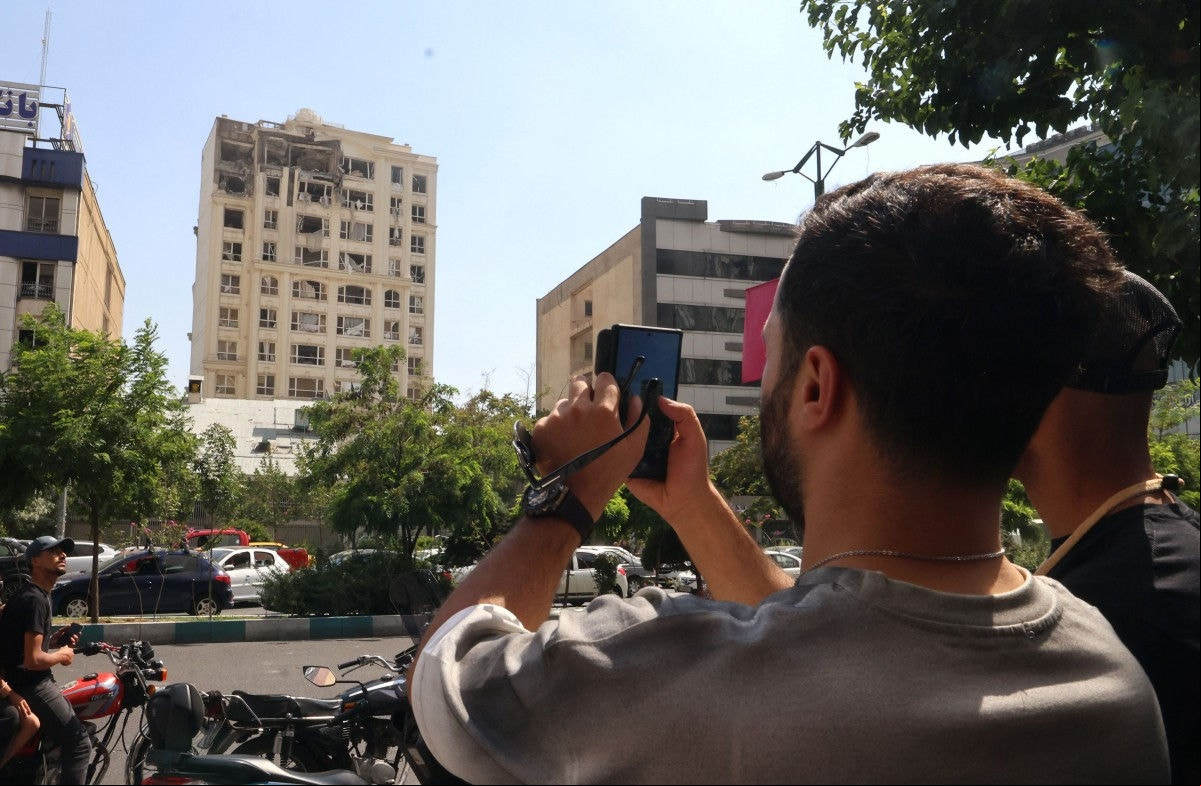 Um homem tira uma foto de um prédio danificado em um ataque israelense a Teerã em 13 de junho de 2025